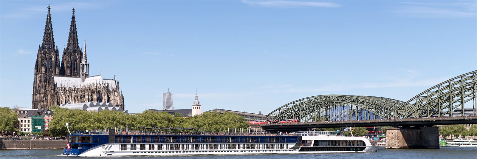 River cruise ship moored on the Rhine in Cologne below the cathedral and a railway bridge