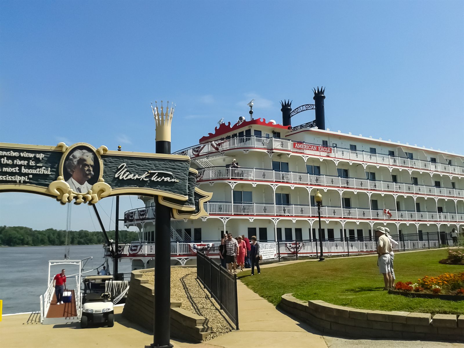 Guests walking from a riverside landing toward a docked paddlewheel riverboat