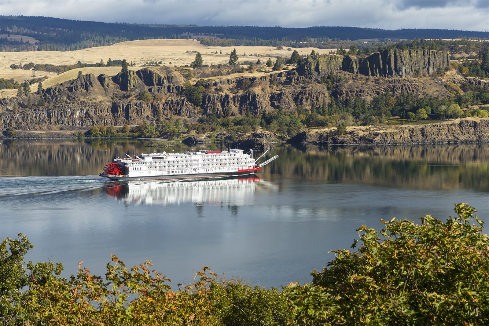 Paddlewheel riverboat cruising below basalt cliffs in the Columbia River Gorge